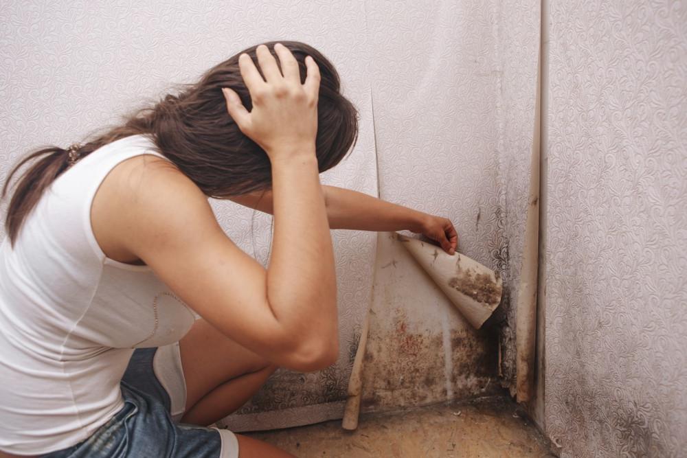 Sad lady looking at mould behind wallpaper